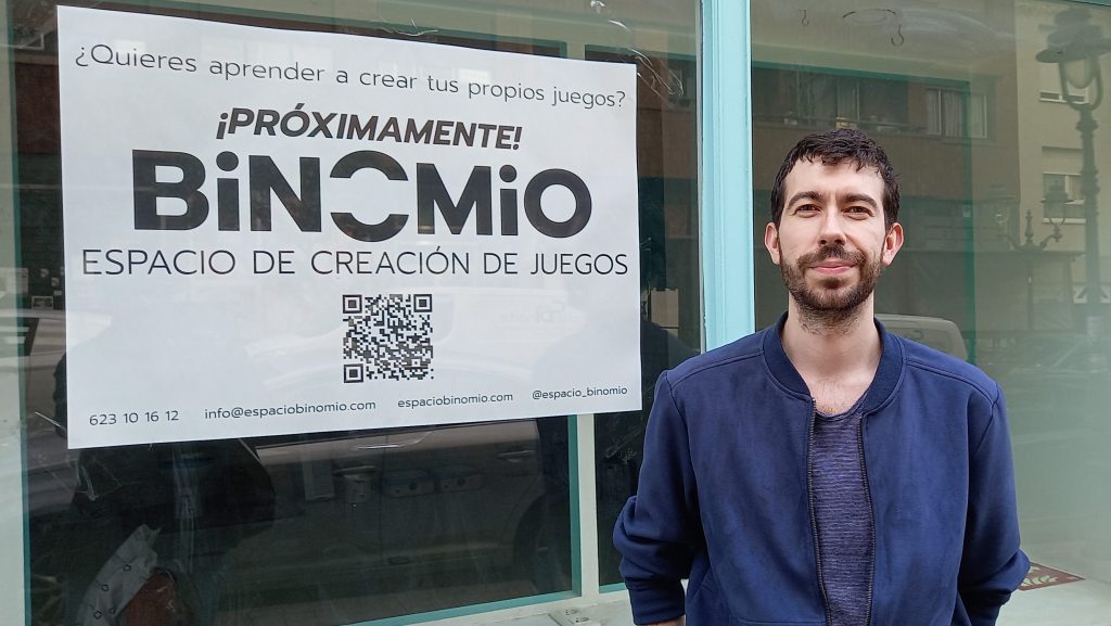 Javier Mombiela delante del escaparate de Binomio con un cartel atrás que dice: Próximamente Binomio, espacio de creación de juegos